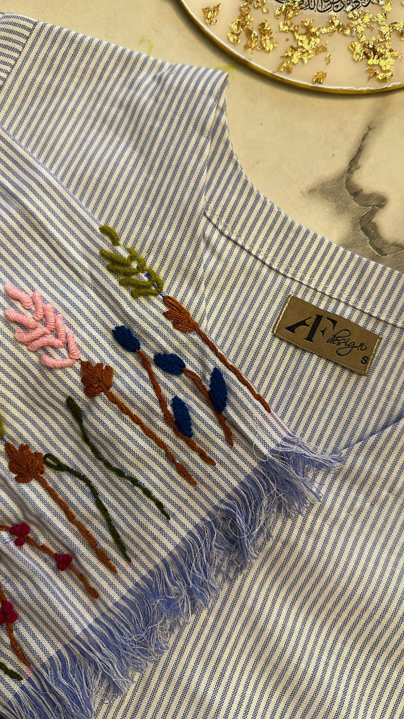 detailing of a sleeve with floral embroidery and tassel fringes on a striped fabric