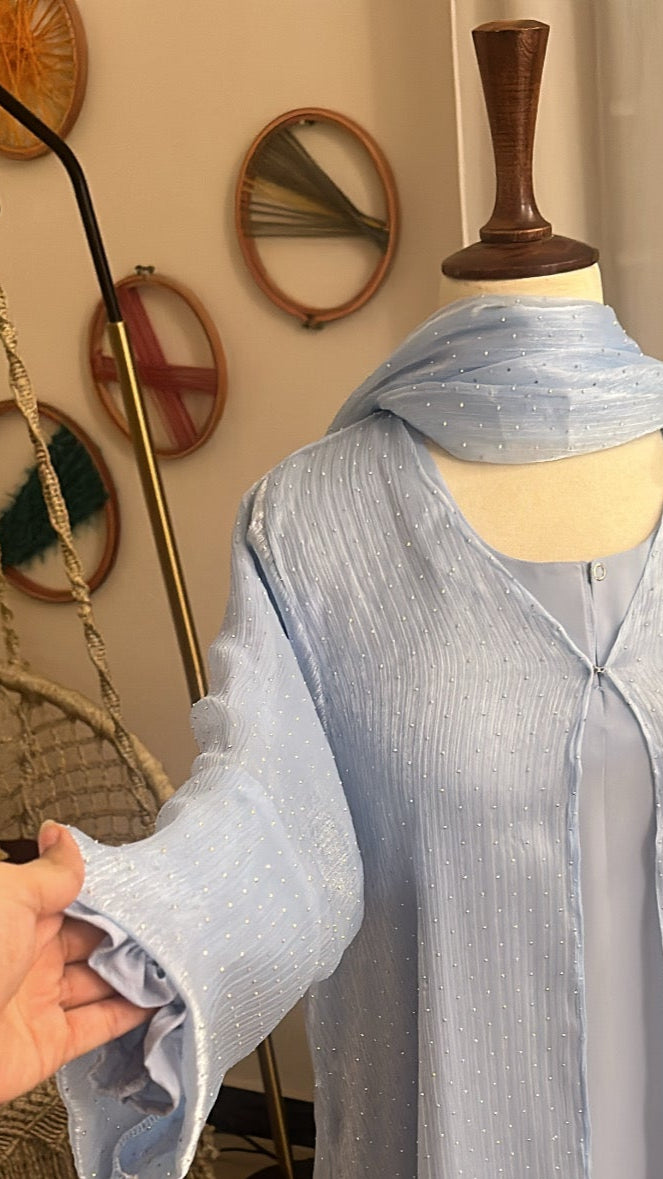 Light blue dress on a mannequin with a hand adjusting it, in a room setting.
