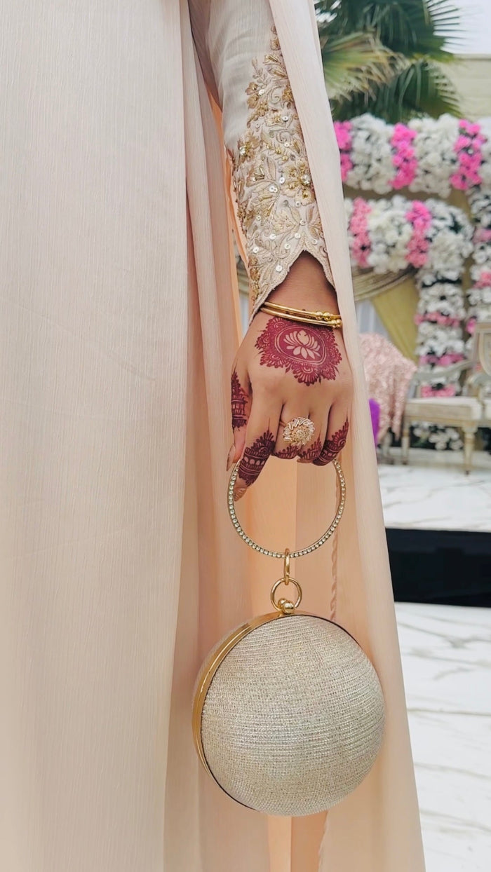 Person holding a round beige handbag with floral design in the background