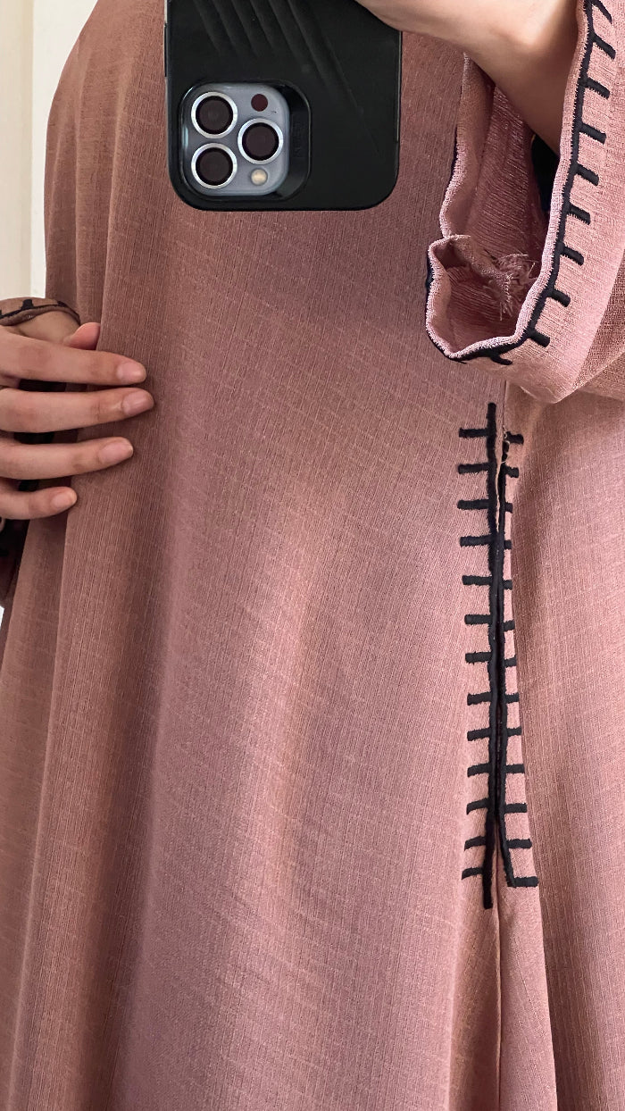 Close-up of a brown fabric with black stitching, held by a hand, with a phone in the corner.