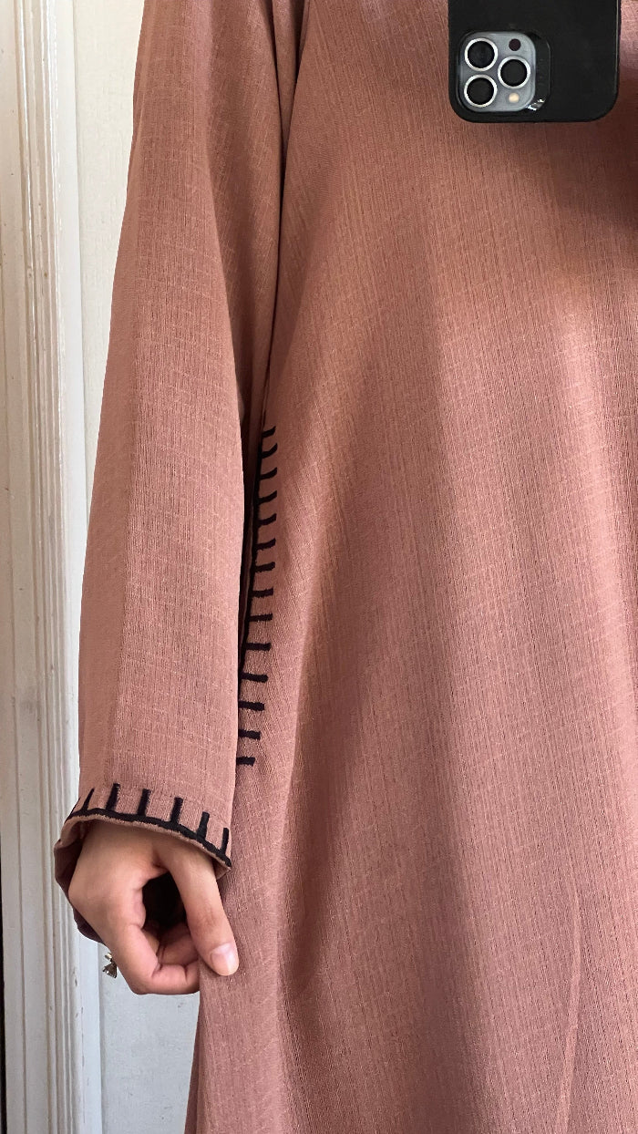 Close-up of a person wearing a pink long-sleeve garment with a textured pattern, held against a neutral background.