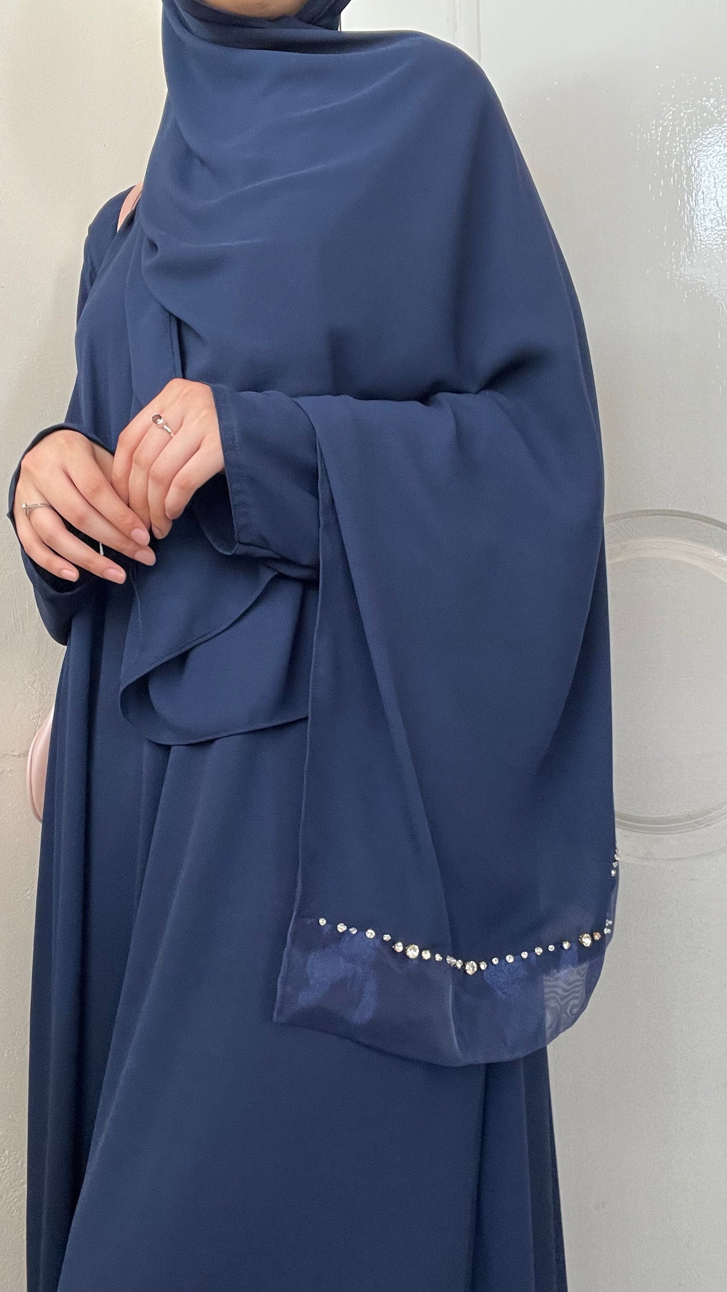 A person wearing a navy blue abaya with a matching inner, standing in front of a door.