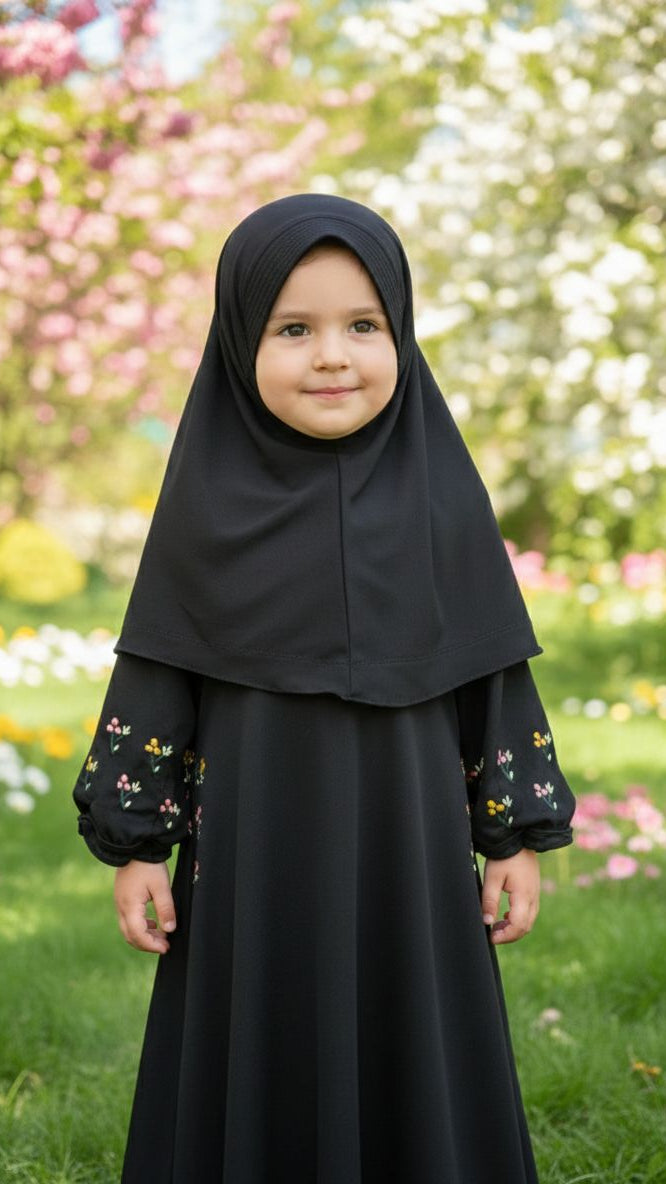 Child wearing a black hijab and dress with floral embroidery in a garden setting