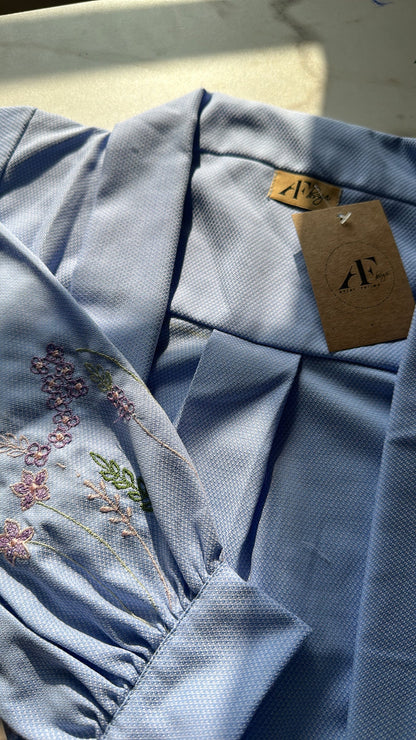Light blue fabric with floral embroidery and a brand tag on a neutral background