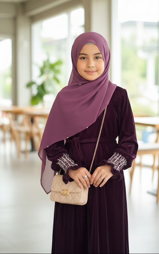 Woman wearing a dark purple hijab and dress in a bright indoor setting