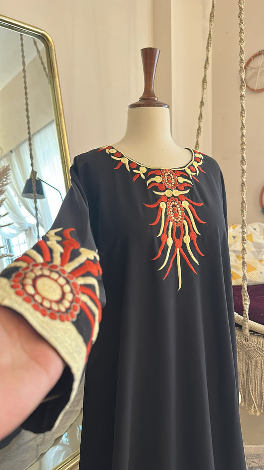 Black dress with colorful embroidery on a mannequin against a neutral wall.