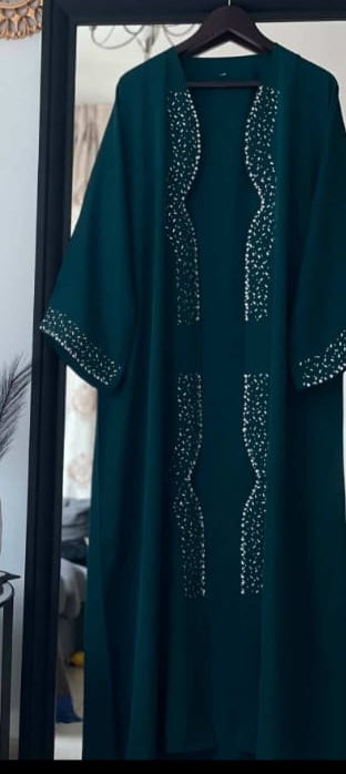 Green abaya with embellishments on a hanger in front of a mirror.