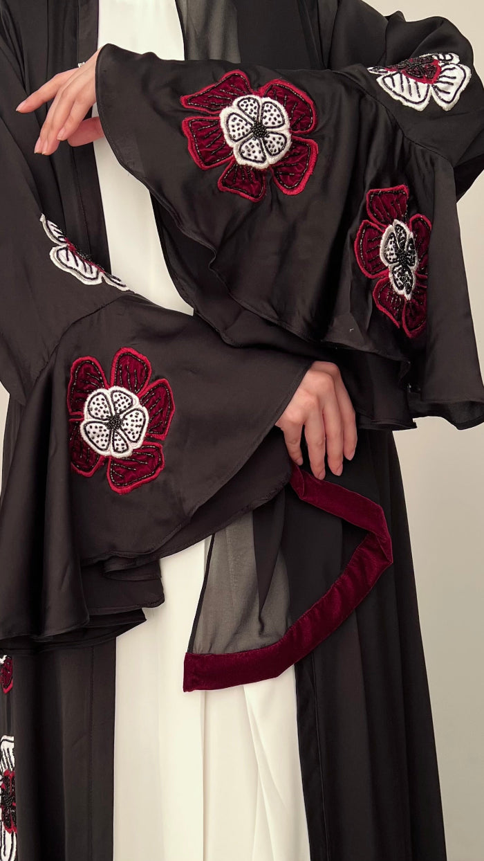 Black abaya with red and white floral embroidery on a neutral background