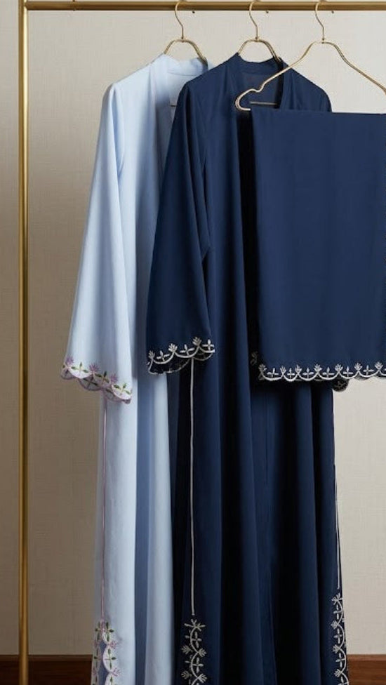 Navy and light blue dresses with intricate detailing on a gold rack against a beige wall.