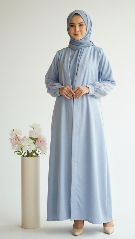 Woman wearing a light blue dress and hijab standing next to a vase with flowers on a white background