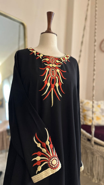 Black dress with red and gold embroidery on a mannequin in a room setting.