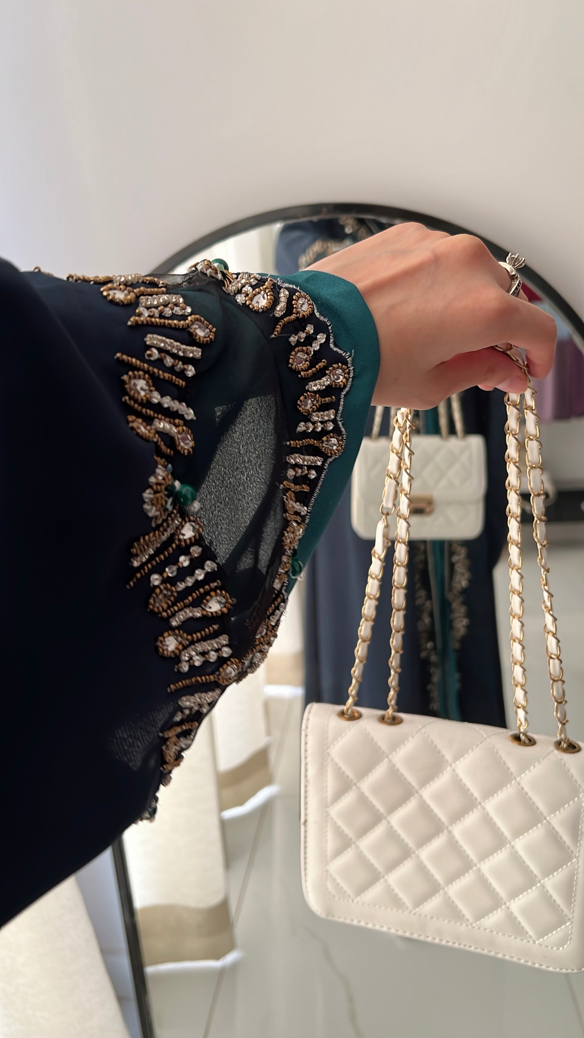 Person holding a white quilted handbag with gold chain strap in front of a mirror.