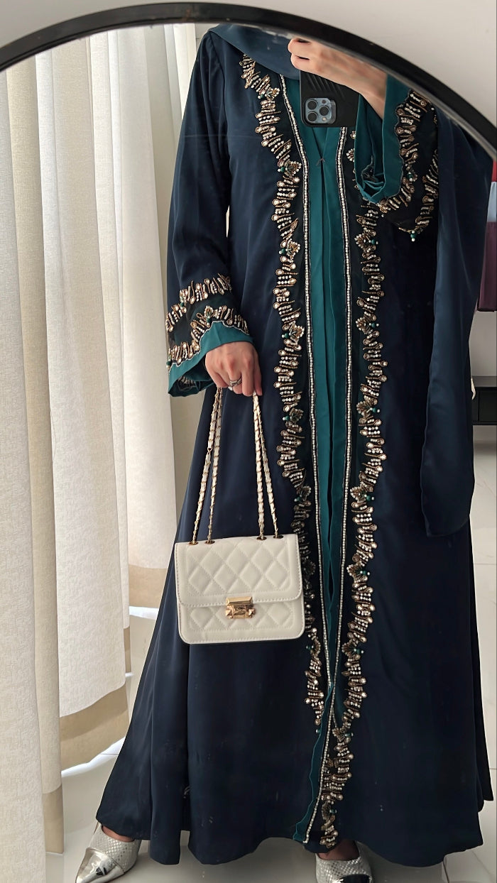 Person wearing a long, dark blue embroidered dress holding a white handbag.
