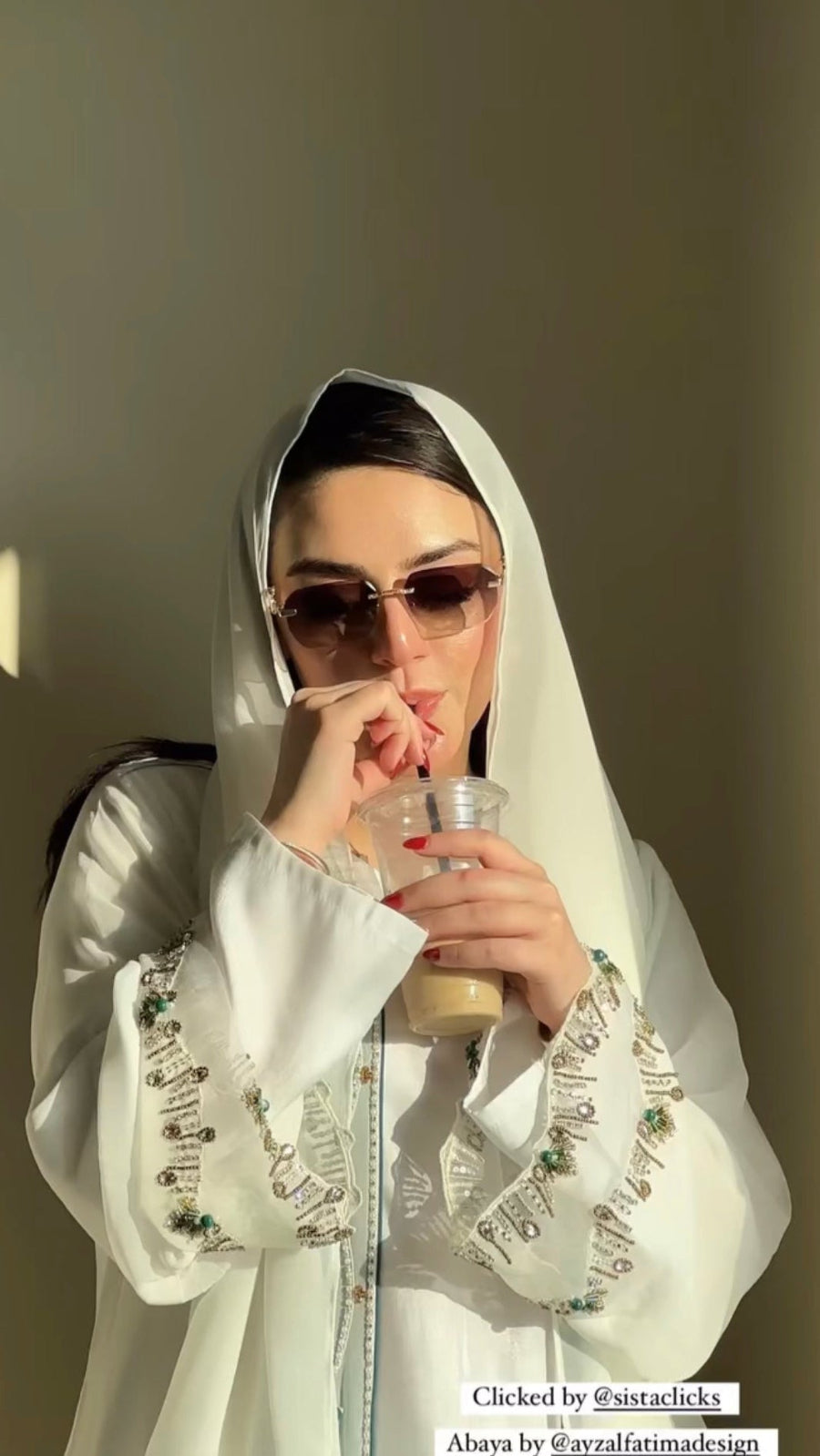 Person wearing a white outfit with intricate patterns, drinking from a cup.