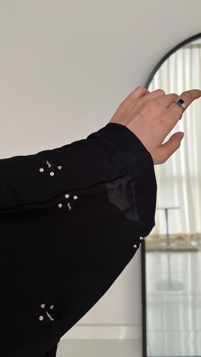 Person wearing a black long-sleeve shirt with pearl-like embellishments, standing in front of a mirror.