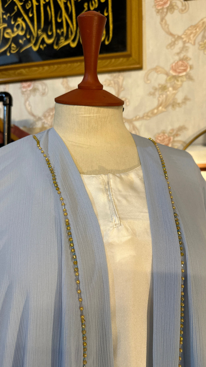 Light blue dress with gold trim on a mannequin against a floral wall.