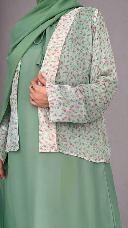 Person wearing a green hijab and a light green dress with a floral patterned shirt.