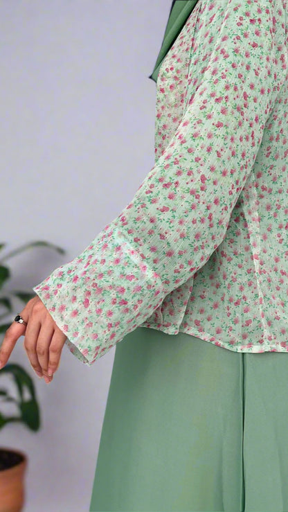 Person wearing a green outfit with a floral patterned shirt against a plain background
