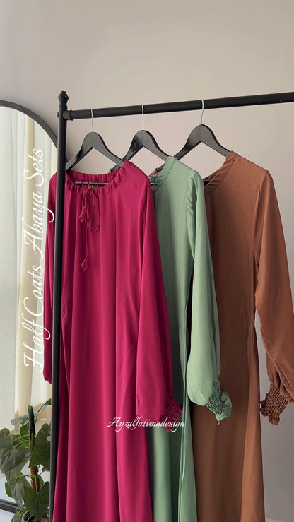 Three dresses in pink, green, and brown hanging on a rack against a white wall.
