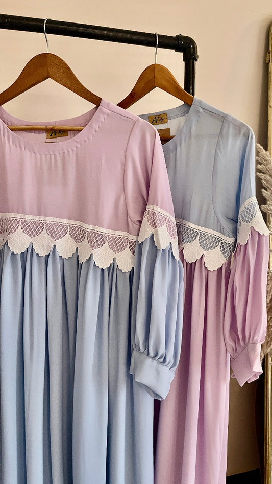 Two dresses, one light blue and one pink, with lace details, hanging on a rack.