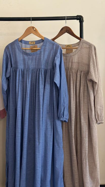 Two dresses, one blue and one brown, hanging on a rack against a beige wall.