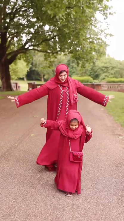 Two people in matching red outfits standing on a path with trees in the background