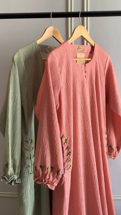 Two dresses, one green and one pink, hanging on a rack against a plain wall.