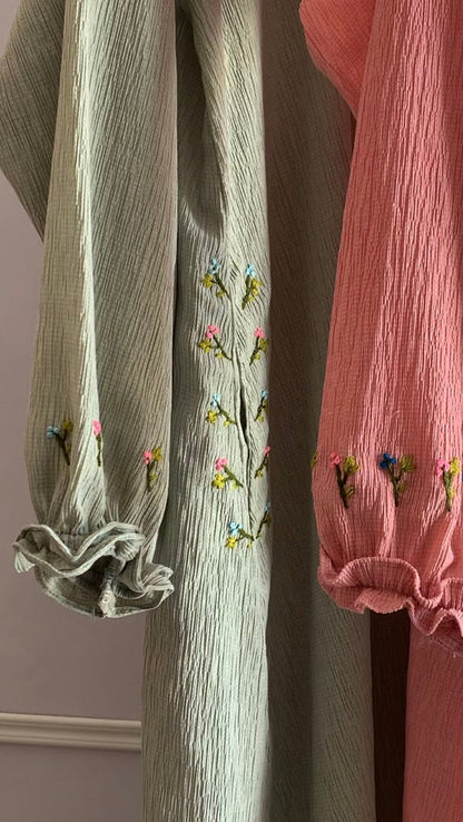 Two pairs of pants, one green and one pink, with floral embroidery on cuffs against a neutral background.