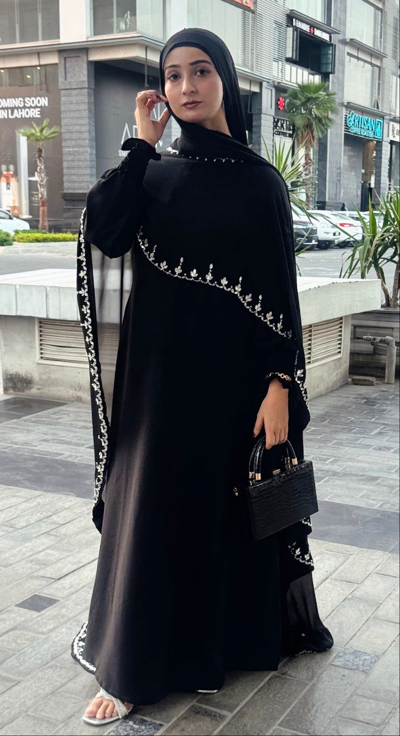 Woman in a black abaya with white embroidery standing on a city street.