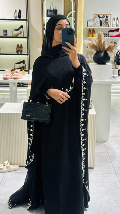 Woman in a black abaya with white embroidery taking a mirror selfie in a store.