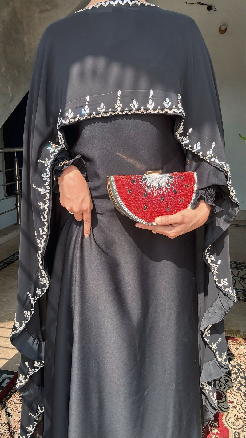 Person wearing a dark gray dress with white embroidery, holding a red clutch with white patterns.
