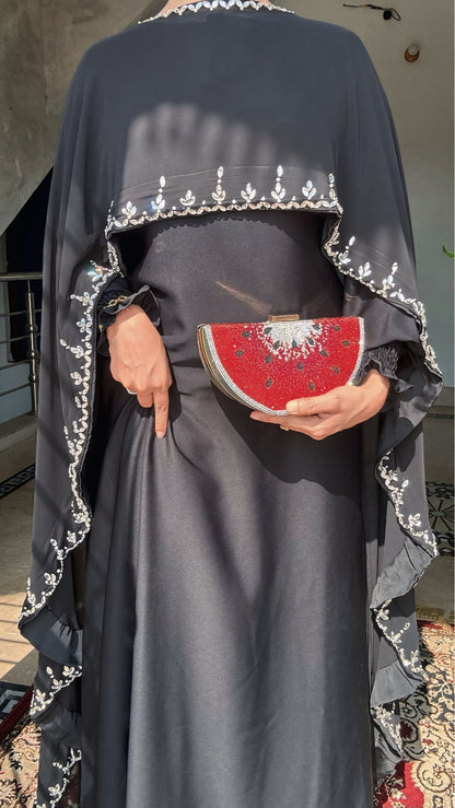 Person wearing a dark gray dress with white embroidery, holding a red clutch with white patterns.