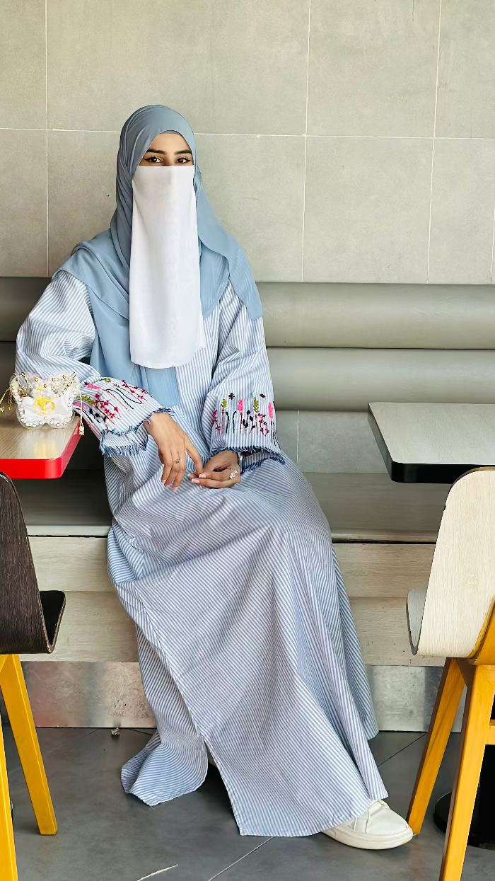 Person wearing a light blue hijab and dress sitting at a table in a casual setting.