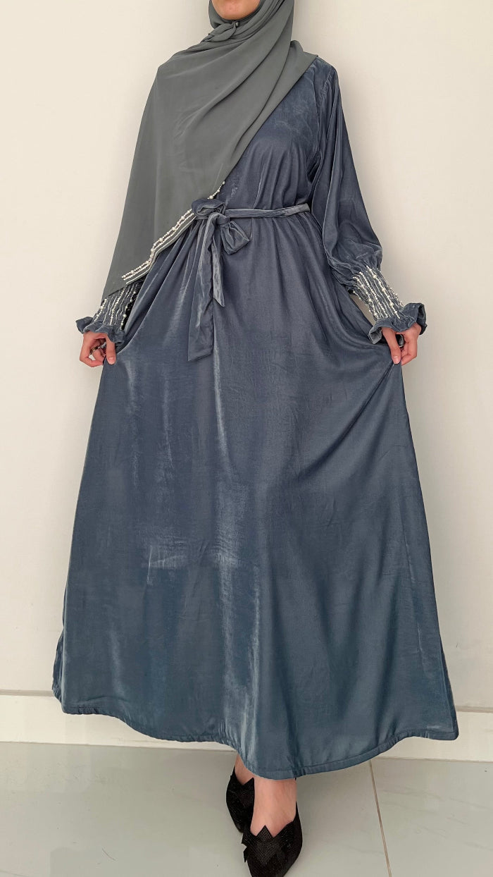 Person wearing a long, dark blue dress with a gray hijab against a plain background