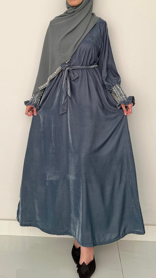 Person wearing a long, dark blue dress with a gray hijab against a plain background