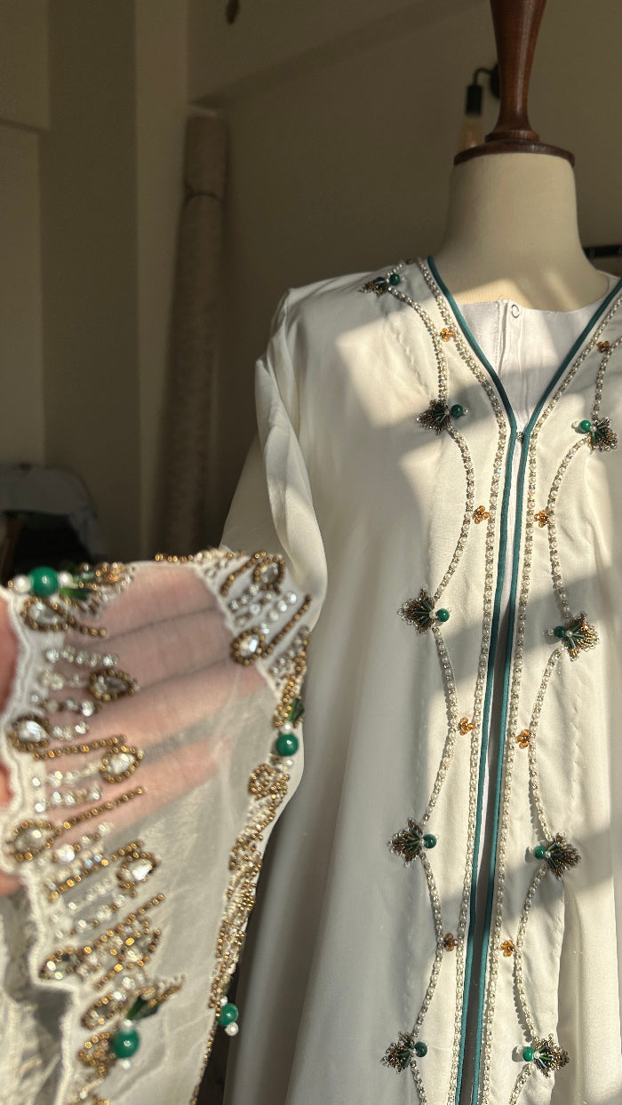 White garment with intricate beadwork on a mannequin against a neutral background