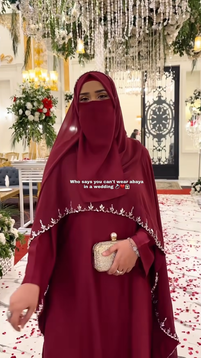 Person wearing a burgundy dress with decorative trim in an elegant indoor setting.
