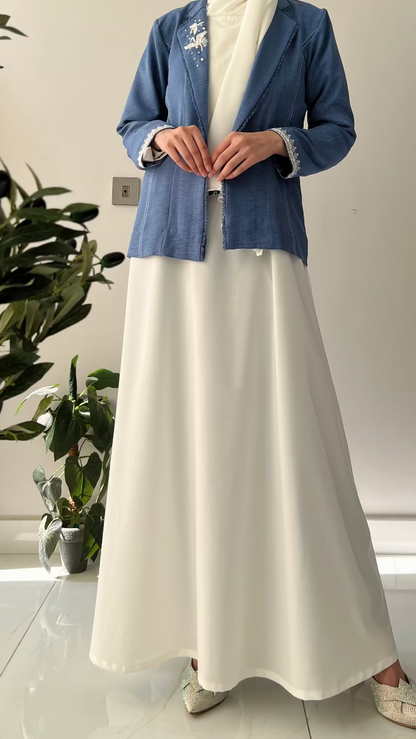 Person wearing a blue jacket and white dress standing indoors with plants in the background