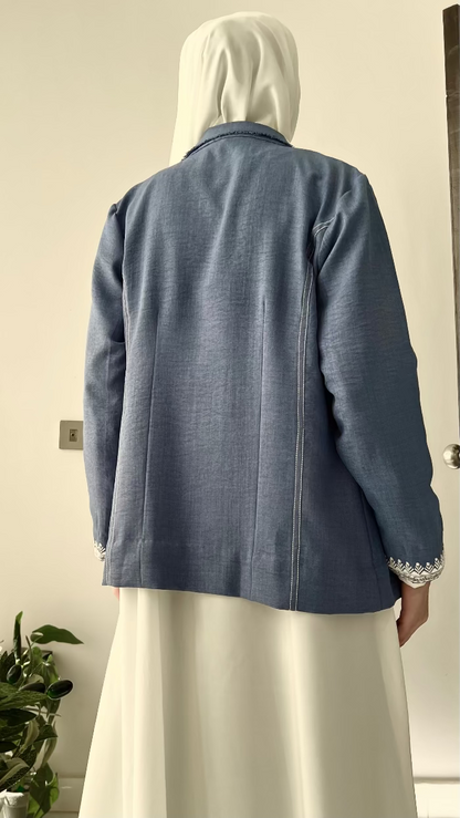 Person wearing a blue jacket with white hijab standing in front of a door.