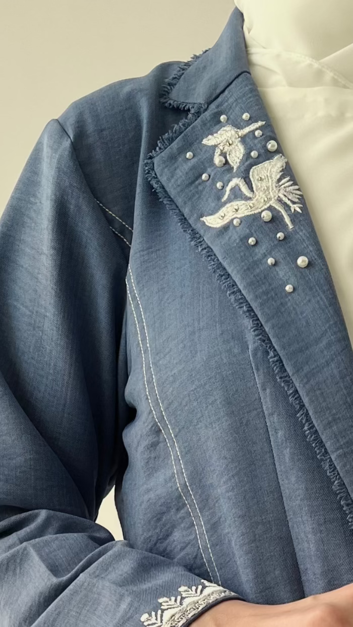Blue denim jacket with white embroidery on a beige background