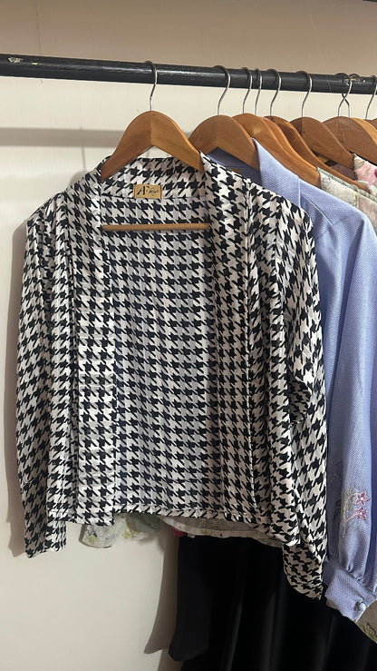 Folded houndstooth pattern fabric on a rack with other fabrics in the background.