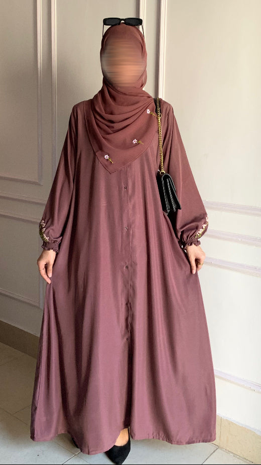 Person wearing a long mauve dress with a hijab in a neutral setting