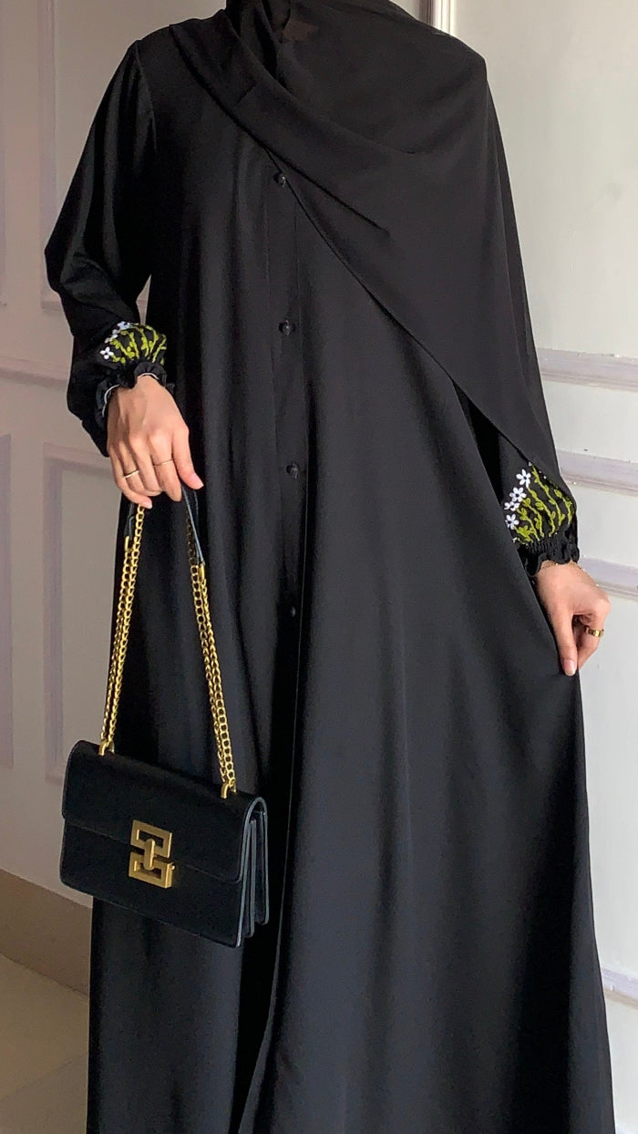 Person wearing a black abaya holding a black handbag with gold chain in a neutral setting