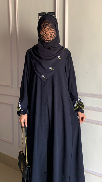 Person wearing a black abaya with floral embroidery in a room with white paneled walls.
