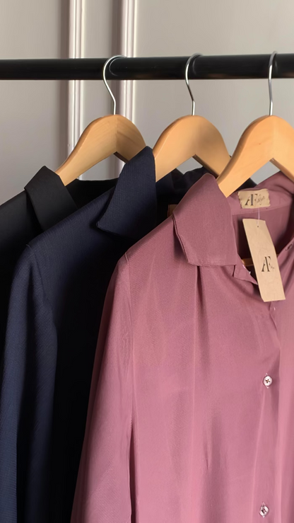 Pink shirt with a tag on a hanger next to a black shirt, against a neutral background.