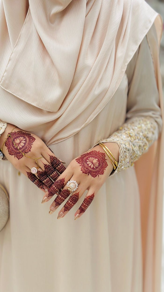 Person wearing a beige hijab and dress with intricate henna designs on hands.