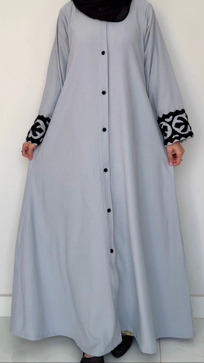 Long light gray dress with black buttons and patterned cuffs on a white background