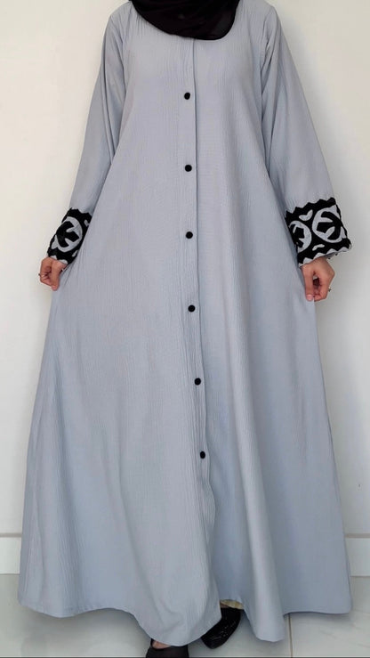 Long light gray dress with black buttons and patterned cuffs on a white background