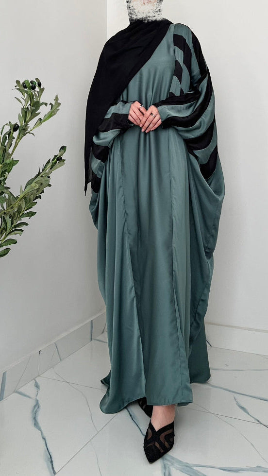 Person wearing a long green dress with a black shawl in a minimalistic room.