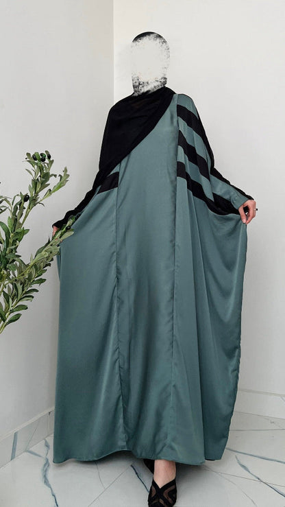 Person wearing a long, dark green dress with a black and gray patterned shawl in a minimalistic setting.